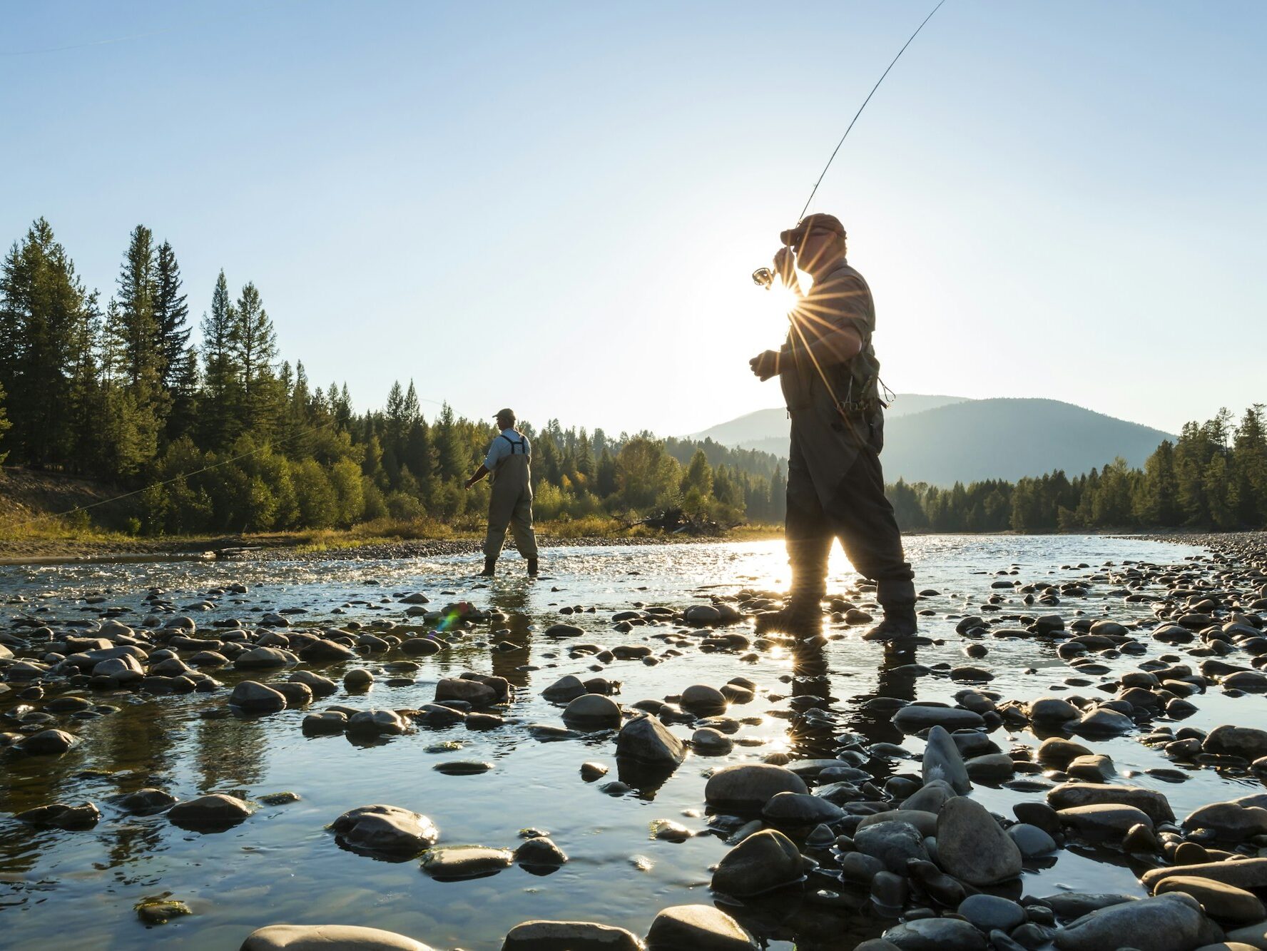 Two fly fisherman standing in rocky riverbed, casting their fishing rods.